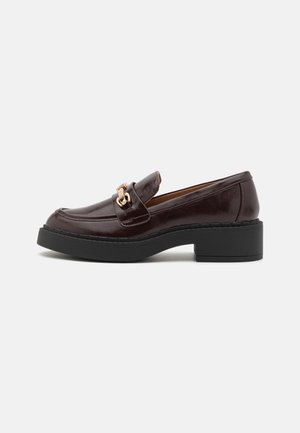 Mørkebrune læder loafers med rundet tå, sort platformsål og guldfarvet hardware-detalje på vristen. Tekstureret finish, afslappet design.