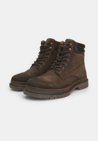 Stivaletti alla caviglia in suede marrone con lacci, occhielli in metallo e suola in gomma testurizzata. Presentano un colletto imbottito e una finitura liscia sulla parte superiore.