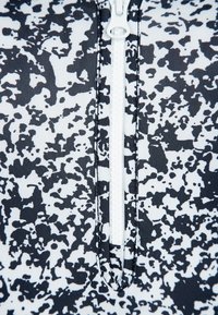 Svart- och vitrandig baddräktstopp med ett abstrakt prickigt mönster, tillverkat av ribbat tyg, med en central vit dragkedja.