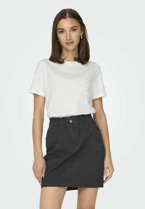 Camiseta blanca con bolsillo texturizado, combinada con una falda negra de cordón con corte recto y cierre de botones en la parte delantera.