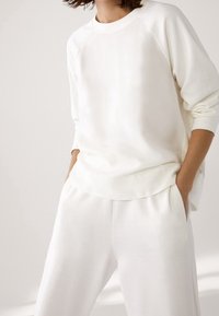 Witte katoenen sweatshirt met raglanmouwen, in combinatie met bijpassende losse witte broek, met een zachte textuur en een elastische tailleband.