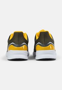 Urheilukengät tumman khakin värisestä verkkomateriaalista, keltaisilla yksityiskohdilla ja valkoisilla pohjilla. Varustettu pyöreällä kantapäällä ja teksturoiduilla pintakäsittelyillä.