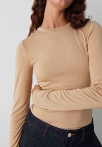 Beige longsleeve t-shirt van gladde stof. Heeft een ronde halslijn en een slim fit ontwerp, gecombineerd met donkere denim.
