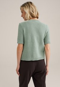 Pull léger à manches courtes en maille texturée vert clair, avec un ourlet et des poignets côtelés, offrant un ajustement décontracté et un subtil motif.