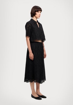 Set din dantelă neagră format din două piese, incluzând un top scurt cu guler și o fustă lungă, ambele cu modele tăiate intricate și margini ondulate.