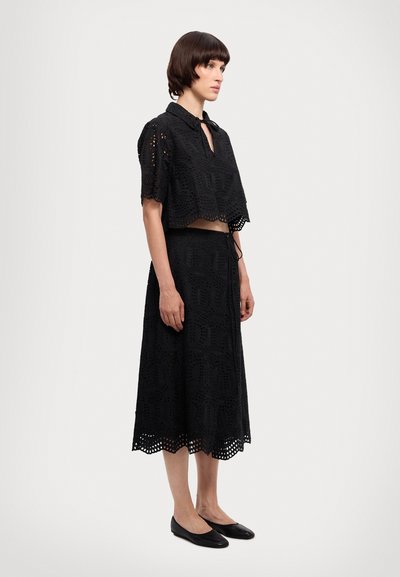 Černý dvoudílný outfit se zkráceným topem s krátkými rukávy a průstřihem ve vzoru očíček, doplněný dlouhou, sladěnou sukní s vroubkovaným lemem.