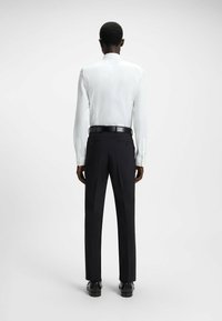 Camicia bianca a maniche lunghe abbinata a pantaloni neri su misura. La camicia presenta un colletto a punta, mentre i pantaloni hanno una vestibilità slim con tasche.