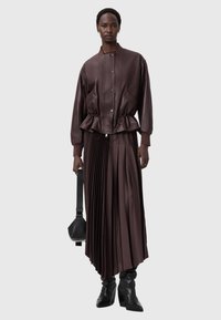 Hnědá kožená bombardérka s plisovanou sukní. Má na sobě úzký pas, žebrované manžety a kapsu. Nošena s kotníkovými botami a malou kabelkou.