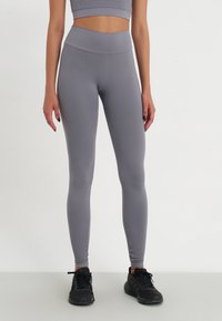 Colanți gri deschis cu un model texturat de fagure, talie înaltă și o croială ajustată, asociați cu pantofi sport negri.