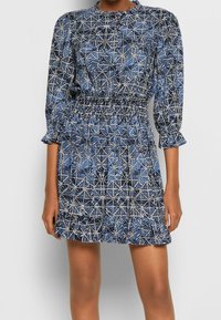 Abito blu e bianco con motivo, maniche lunghe, vita smock e polsini volanti, caratterizzato da un design geometrico e un tessuto leggero.