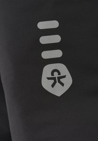 Svart tyg med ett ljusgrått emblem som har en sköldkontur och en tillgänglighetssymbol, åtföljd av tre horisontella grå linjer ovanför.