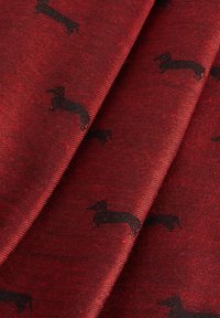 Rødt stof med en struktureret overflade, der har et gentaget mønster af små sorte dachshunde. Blødt og fleksibelt materiale, egnet til tøj eller accessories.