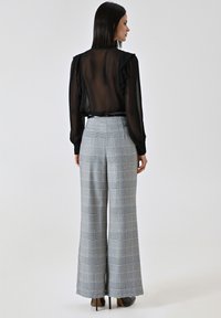 Zwarte, doorschijnende blouse met geplooide mouwen. Grijs geruite hoge taille wijde broek met een soepele textuur en een losse pasvorm.