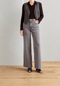 Szary kamizelka na czarnej bluzce z długim rękawem, w połączeniu z szarymi dżinsami o wysokim stanie i szerokimi nogawkami oraz butami na obcasie z blokiem z srebrnymi akcentami.