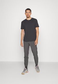 Czarna koszulka z krótkim rękawem w połączeniu z szarymi zwężanymi joggerami. Joggersy mają kieszenie i czarne mankiety. Stylowe buty sportowe w odcieniach szarości i czerwieni dopełniają stylizację.