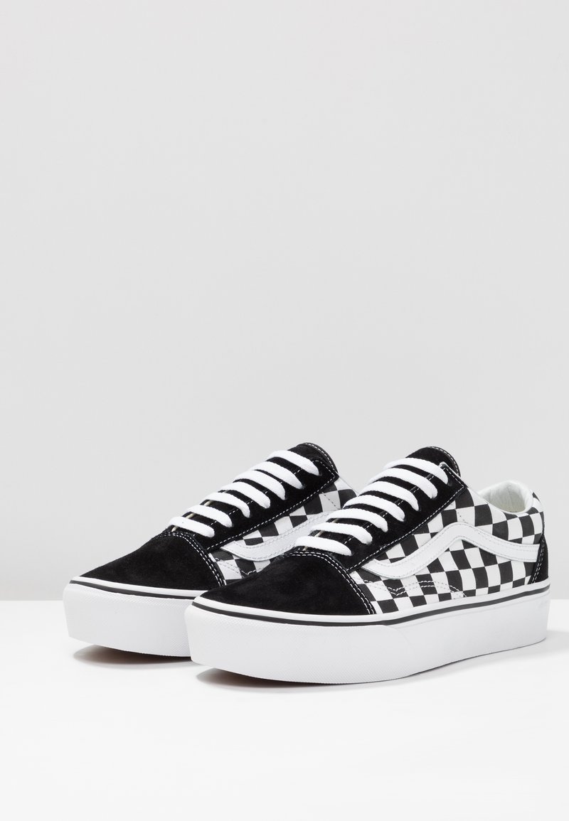 Zapatillas de lona en blanco y negro con diseño de tablero de ajedrez, detalles de ante, cordones blancos y suela de goma con un diseño ligeramente elevado.