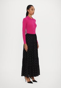 Fuchsia stickad cardigan med knappstängning, ihop med en svart, plisserad kjol med vita prickar och svarta spetsiga klackar.