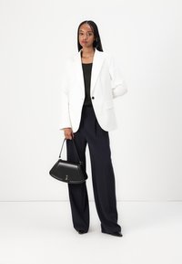 Bílý blazer, černý top a navy široké kalhoty. Černá kabelka trojúhelníkového tvaru. Hladké textury a dobře padnoucí střih.