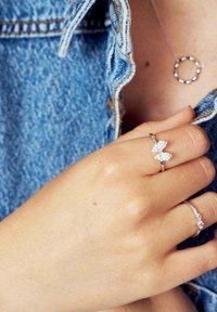 Silverringar med blommönster och geometriska mönster, prydda med klara ädelstenar, bärs på en hand mot en bakgrund av denim.