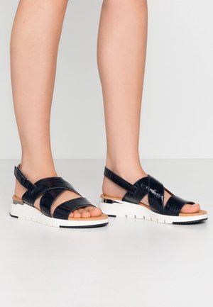 Black patent leather sandals with crisscross straps, open toe design, and a white chunky sole featuring a silver accent.