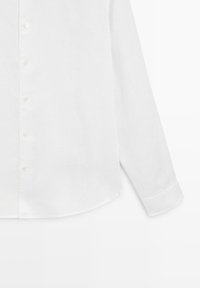Chemise blanche à manches longues avec col classique et boutons blancs sur le devant, montrée de la taille jusqu'au poignet.