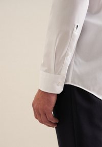 Witte dress-shirt met een puntkraag, manchetten met één knoop en een zwart bloemenborduursel op de mouw. Glad textuur, getailleerd ontwerp.