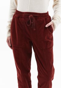 Červené kordové kalhoty s elastickým pasem, detailem na stahování, bočními kapsami a uvolněným střihem, s vertikálními švy jako dekorací.