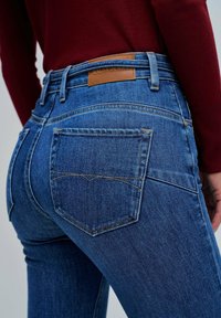 Jeans in denim blu con una vestibilità a vita media, caratterizzati da un'etichetta in pelle sul retro, cuciture curve al cavallo e cuciture a contrasto sulle tasche.
