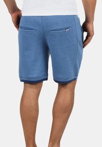 Pantaloni sportivi blu con una texture liscia, caratterizzati da un orlo e tasche posteriori in contrasto navy, logo del marchio sul lato destro.