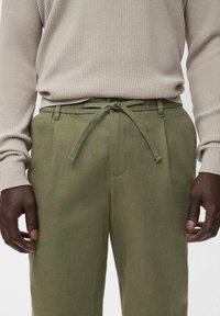 Pantalones de mezcla de lino en verde oliva, con cintura con cordón, bolsillos laterales y un corte relajado, combinados con una camiseta de manga larga acanalada en beige claro.