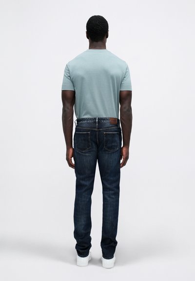 Temno modri jeans in svetlo modra majica. Jeans imajo rjavo usnjeno nalepko in vidno šivanje. Rez je ozek.