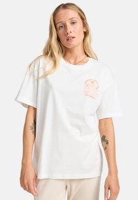 Weißes Baumwoll-T-Shirt mit kurzen Ärmeln, rundem Halsausschnitt und einem pinken Grafikdruck auf der linken Brust. Enthält Text und ein Palmen-Design.