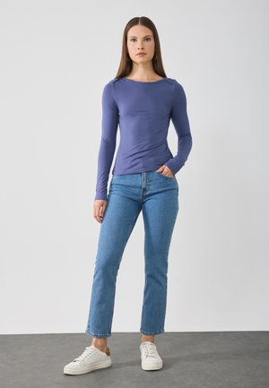 Langermet lilla topp med rund halslinning, sammen med lyseblå rette jeans og hvite sneakers. Enkel og tettsittende design.