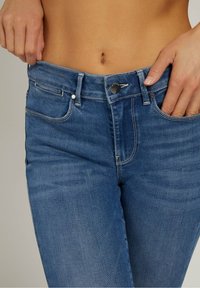 Jeans de mezclilla azul claro con talle medio, cinco bolsillos y cierre de botón metálico. Textura suave con un leve desgastado y detalles de costura.