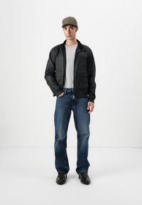 Black bomber jacket with zipper, gray t-shirt, blue jeans, and black boots. Accompanied by a brown plaid cap. Smooth texture, casual fit.