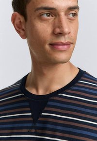 T-shirt rayé en bleu marine, marron et blanc ; encolure ronde ; manches courtes ; tissu doux avec une texture subtile. Couture accentuée à l'encolure.