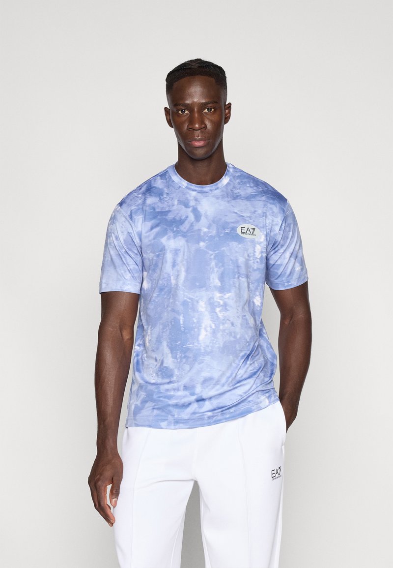 Μπλε μπλουζάκι με φανέλα tie-dye από απαλό ύφασμα, με στρογγυλή λαιμόκοψη και κοντά μανίκια. Λογότυπο EA7 στο αριστερό μέρος του στήθους. Λευκό παντελόνι.