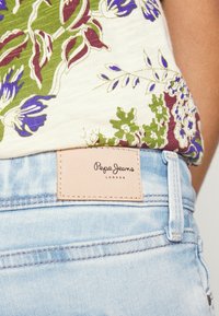 Hedvábná top s květinovým vzorem v zelené, fialové a bílé barvě; světle modré denimové šortky s béžovým koženým logem od Pepe Jeans.