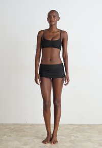 Schwarz Badeanzug mit zwei Teilen, bestehend aus einem Bralette-Oberteil mit dünnen Trägern und einem hochtaillierten Rock, gestaltet mit einer glatten Textur.