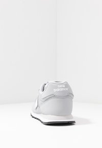 Grau Sport-Schuh mit einem synthetischen Obermaterial, Mesh-Details, gepolstertem Kragen und weißem Logo auf der Ferse. Weiße Zwischensohle und schwarze Außensohle.
