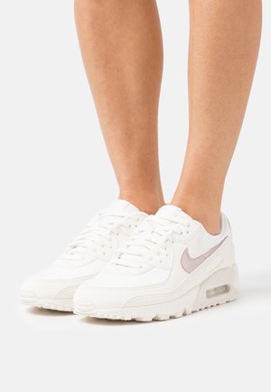 White Nike sneakers with a textured upper, designed with a light pink swoosh accent, lace-up closure, and visible air cushioning.