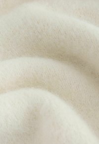 Soft, creamy white wool fabric with a fuzzy, textured surface and gentle folds creating a smooth, cozy appearance.
