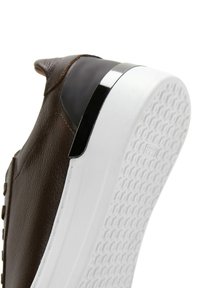 Brown leather sneaker with a black heel accent, white rubber sole featuring a textured pattern, lace-free design, and smooth finish.