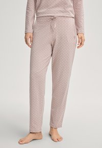 Vrouw in een lichtroze, gemusterd, langemouwen top en bijpassende drawstring broek, staand op blote voeten tegen een neutrale achtergrond.