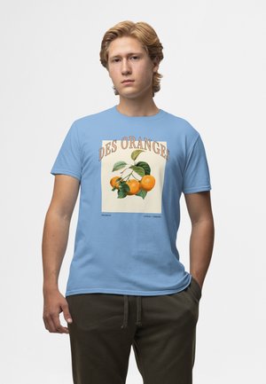 T-shirt en coton bleu clair avec une illustration de fruit orange accompagnée de feuilles vertes et le texte "DES ORANGES" dans un style vintage.