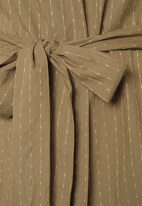 Vestido de tecido verde-azeitona com riscas brancas verticais, apresentando um cinto amarrado na cintura e uma textura suave.