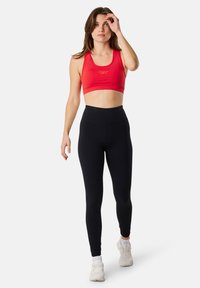 Punainen urheilullinen crop-top ja korkeavyötäröiset mustat legginssit. Topissa on pyöreä kaula-aukko, kun taas legginssit ovat sileät ja joustavat.