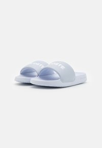 Lyseblå slidesandaler med en struktureret, mat overflade. Har et bredt bånd med "LACOSTE" logoet og en polstret sål.