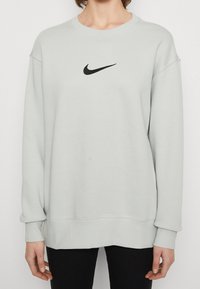 Ljusgrå sweatshirt med en svart Nike-logotyp i centrum, med avslappnad passform, ribbade ärmslut och mjuk, slät tygstruktur.