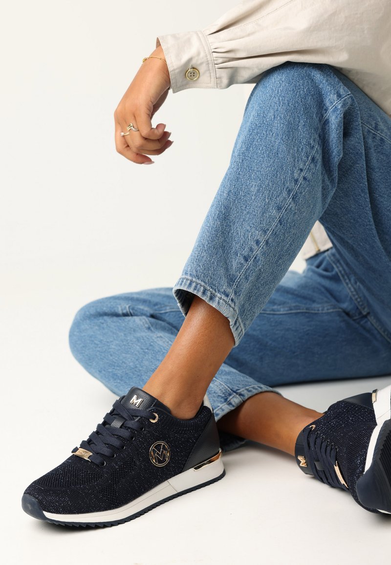 Marinblå sneakers med texturerat stickat övre, guldfärgade detaljer och vit sula. Snörningsdesign med logotypdetalj på sidan.